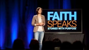 Woman speaking on stage with "Faith Speaks" in the background