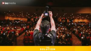 A man holding a camera takes a photo of a theater audience