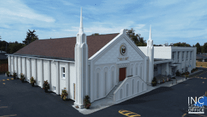 A worship building with steeples, freshly painted and stuccoed in neutral tones with a brown roof.