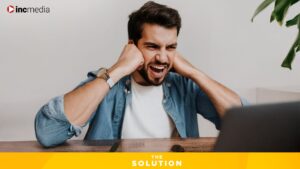 A man looks quite angry while resting his elbows on a desk and his fisted hands on his cheeks.