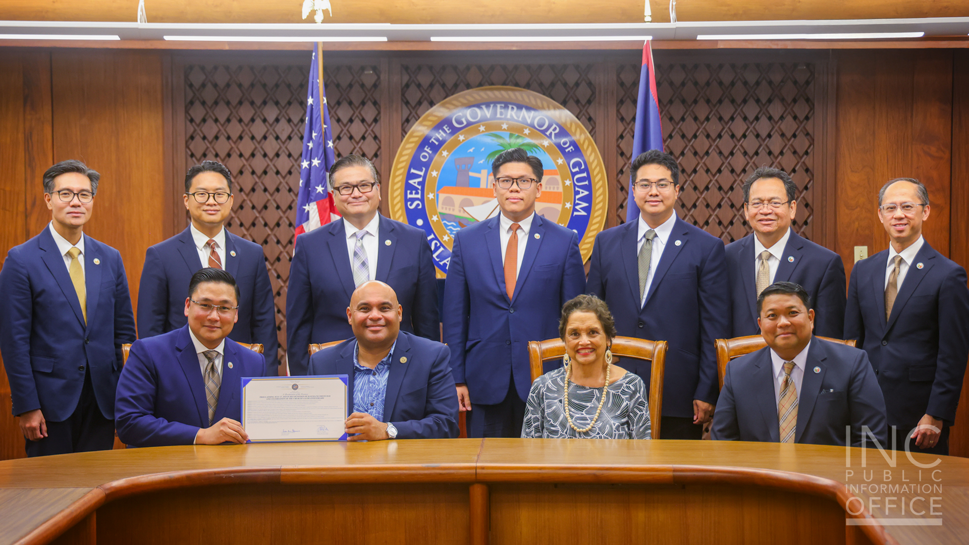 The group sits and stands in two rows while holding up the Governor’s proclamation document.