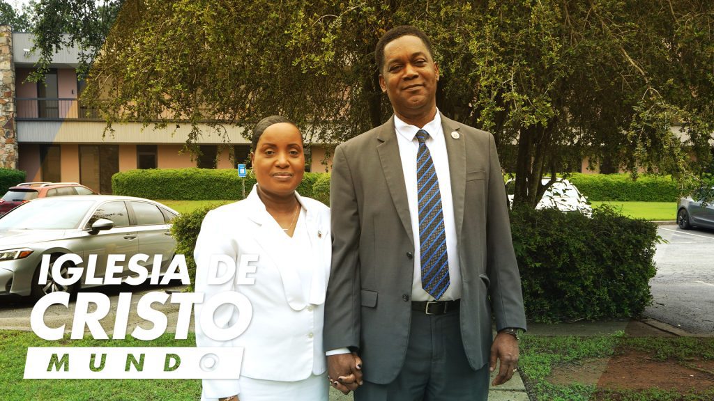 Couple in front of office building in between tree and cars.